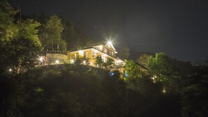 Ein zweistöckiges Haus mit Balkon, umgeben von Bäumen und beleuchtet durch eine einzelne, helle Lichtquelle.