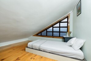 Una habitación pequeña con cama individual, techo inclinado y ventana.