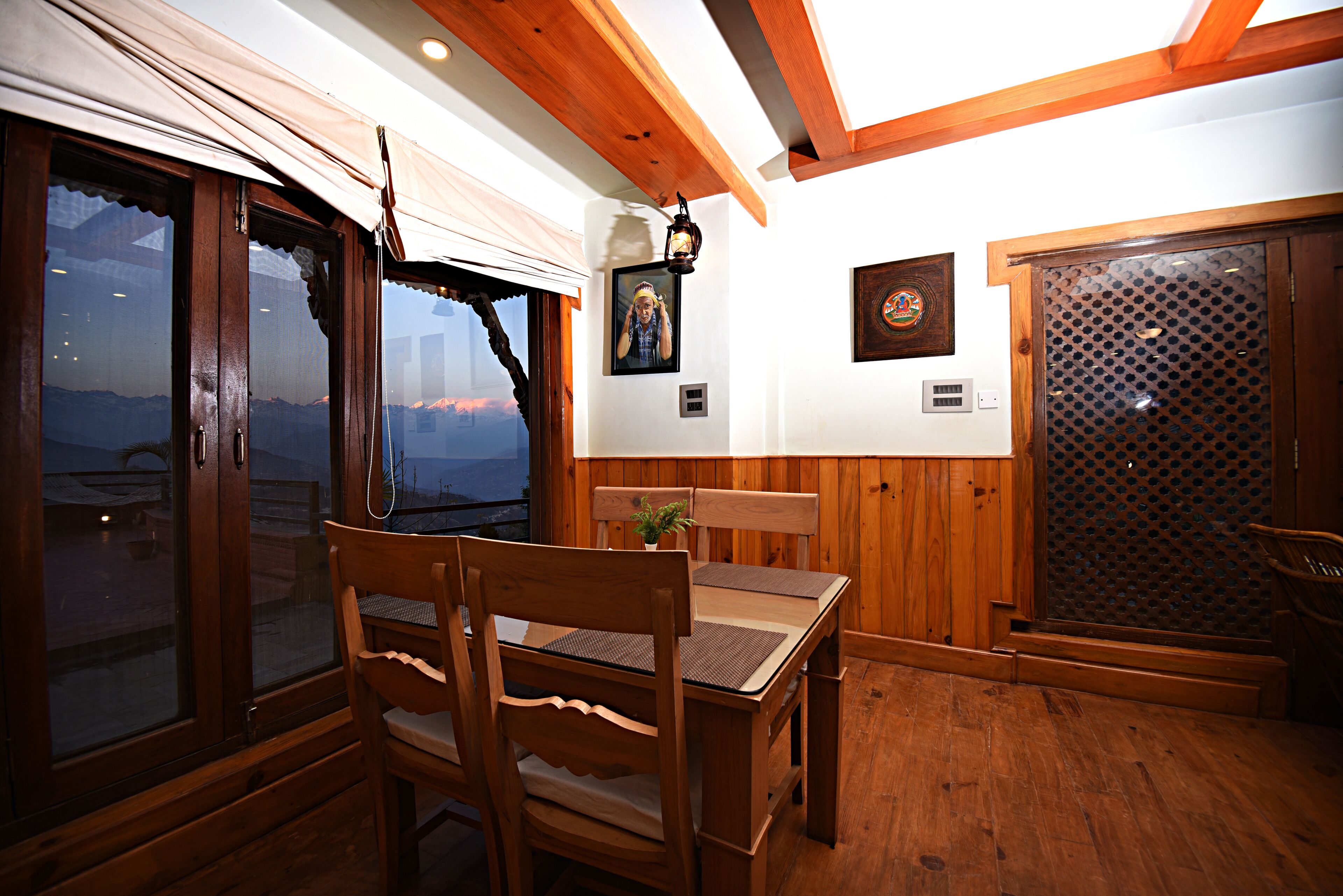 Un comedor de madera con una mesa y sillas, vista a través de un ventanal grande, y techo de madera.