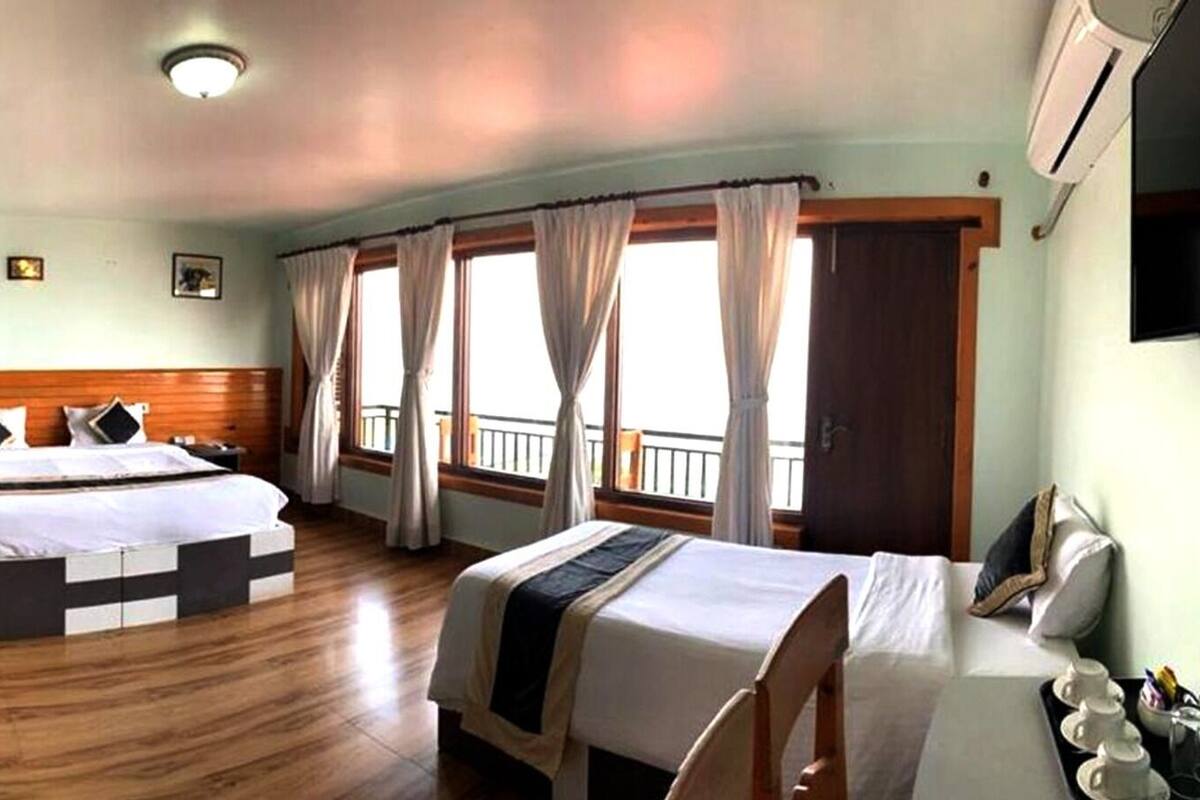A hotel room with two beds, a wooden floor, a balcony with curtains, and a ceiling fan.