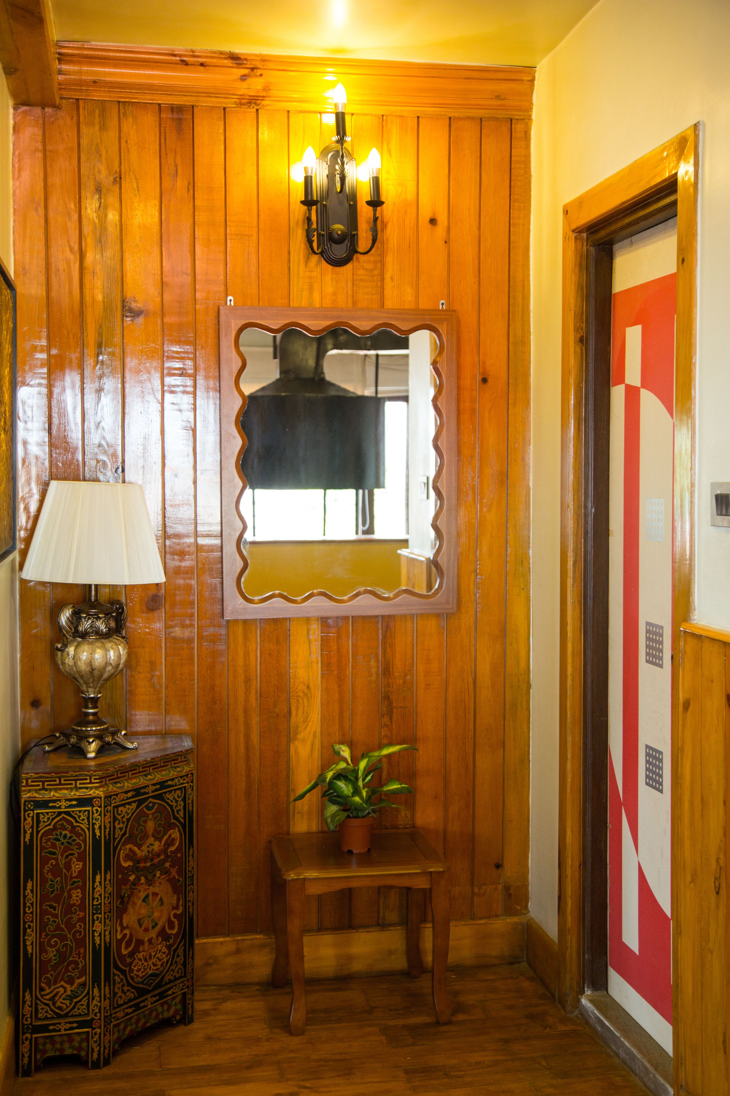 A wooden-paneled hallway with a decorative lamp, a mirror, and a small table with a plant.
