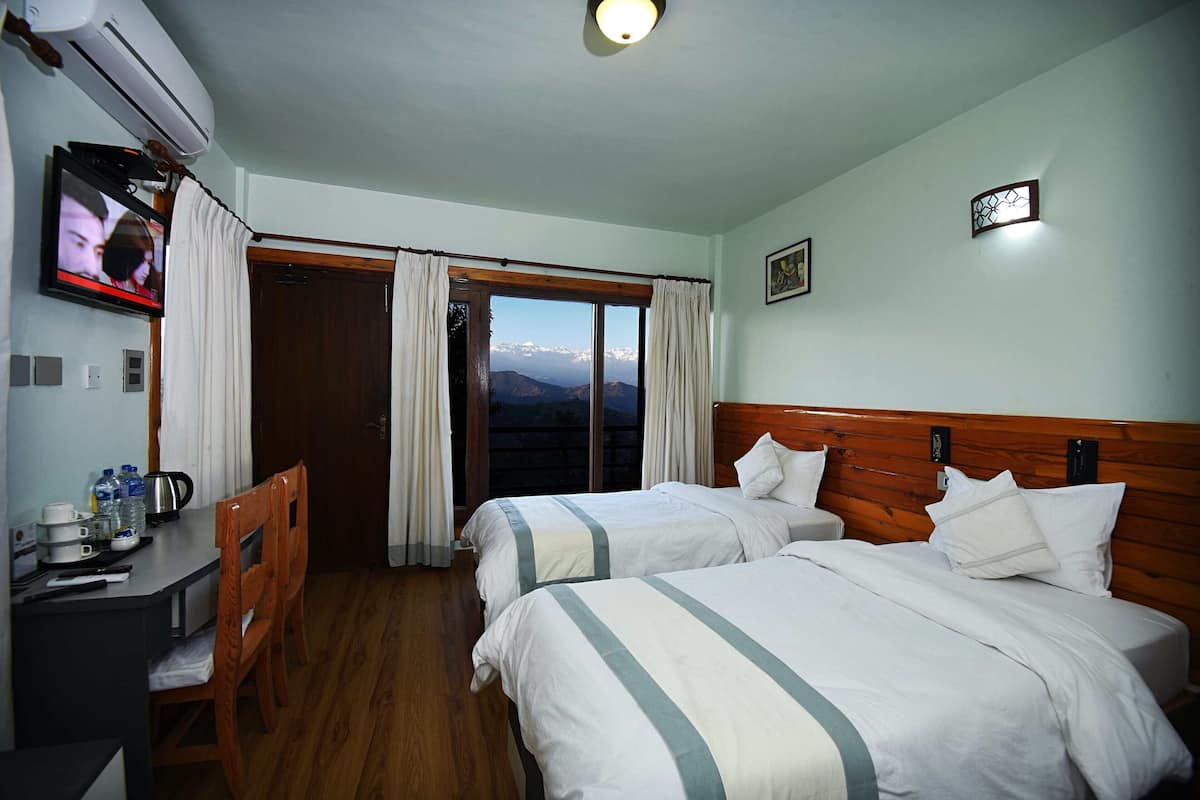 A hotel room with two beds, a desk with a chair, a television, and a view of mountains.