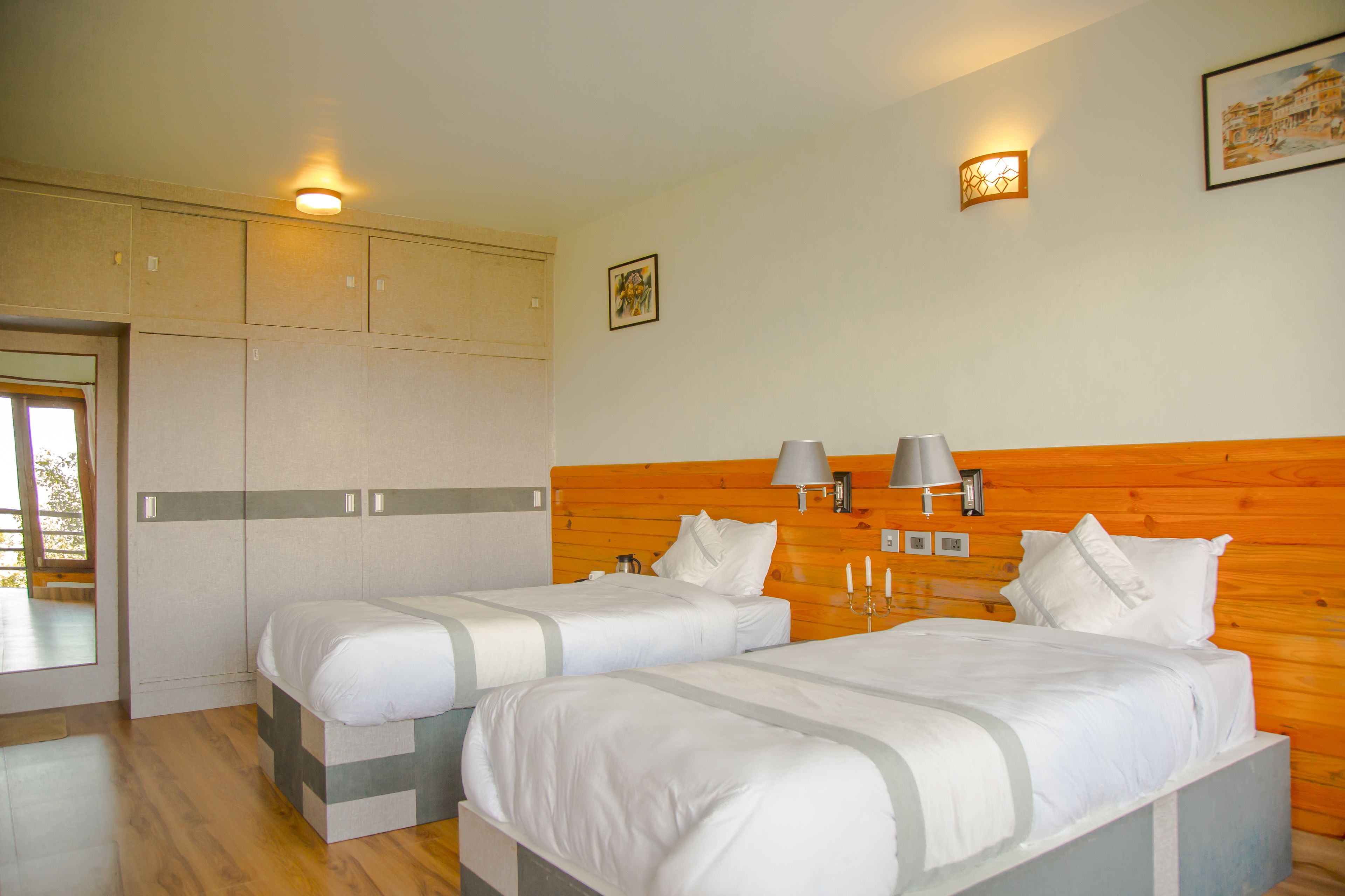 A hotel room with two beds, wooden headboard, bedside lamps, and a large window.