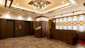 A spacious lobby with a patterned floor, wooden reception desk, and a ceiling light fixture. - KOKO HOTEL Akabane Station (Tokyo)