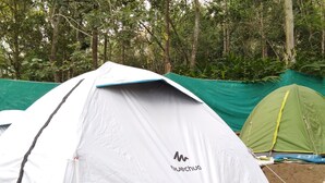 Una tenda bianca con bordi blu e un logo, situata in una zona boschiva con un'altra tenda verde nelle vicinanze.