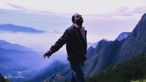 Una persona in piedi sulla cresta di una montagna, con vista su una valle e montagne lontane.