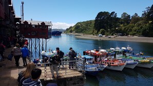 Una zona ribereña con barcos amarrados, un muelle con gente y un edificio de tejado rojo.