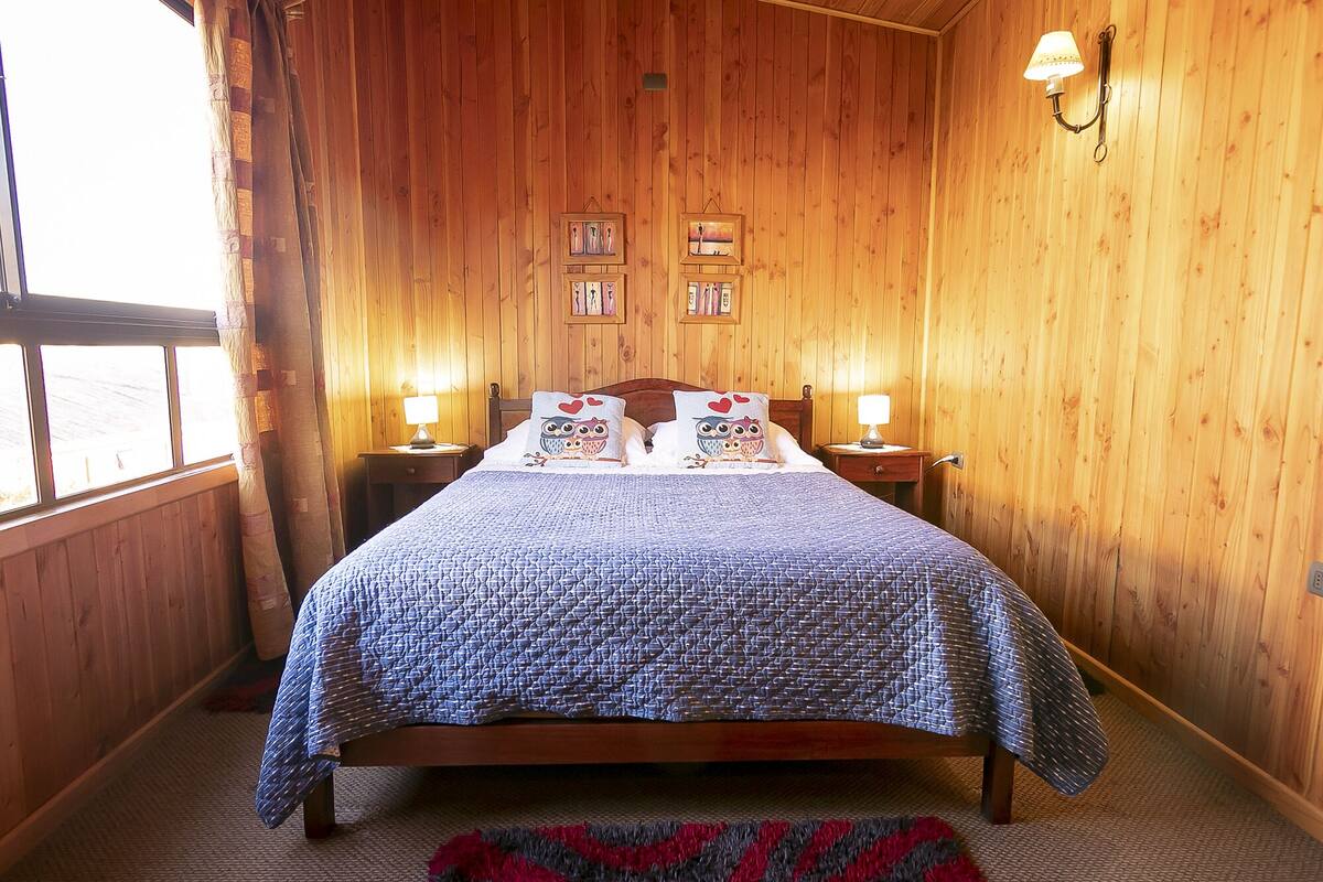 A wooden-paneled room with a bed, two bedside lamps, and framed pictures on the wall.