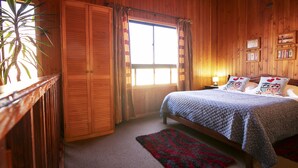 Una habitación de madera con una cama, una ventana con cortinas, una planta y adornos en la pared.