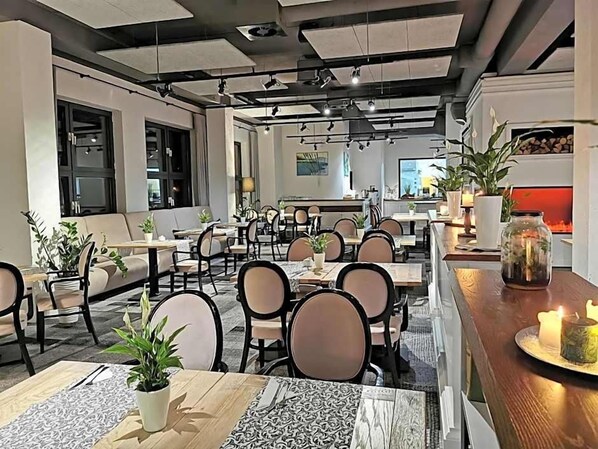 Un comedor moderno con varias mesas y sillas, una zona de bar con mostrador, y plantas en macetas.