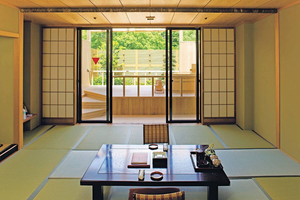 Una habitación japonesa tradicional con suelo de tatami, una mesa baja con juego de té y puertas correderas que dan a un espacio exterior.