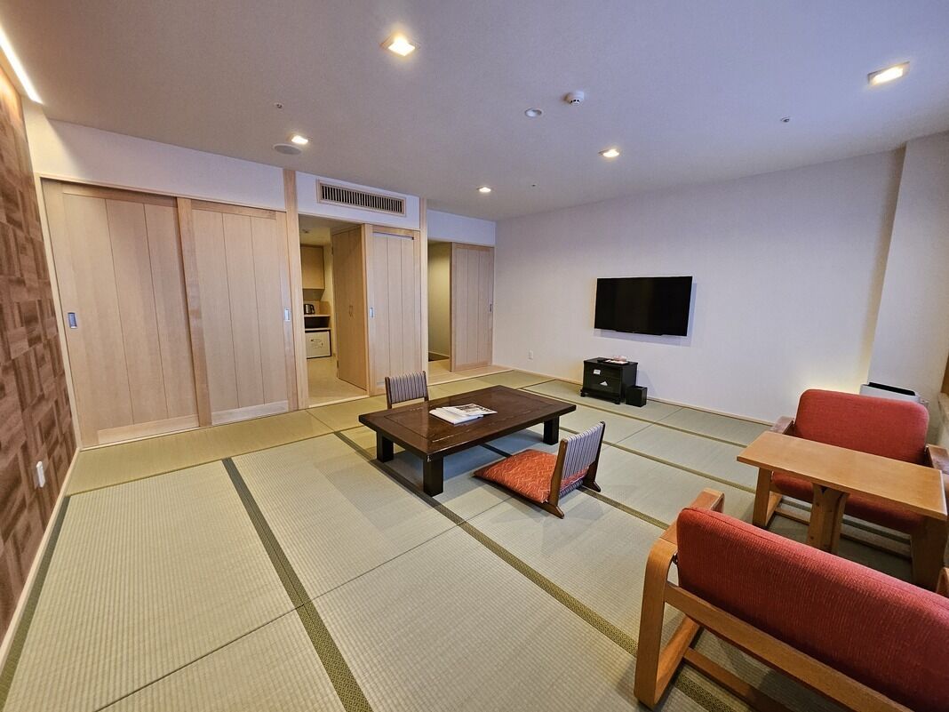 A room with tatami flooring, a low table, chairs, a television, and sliding doors.