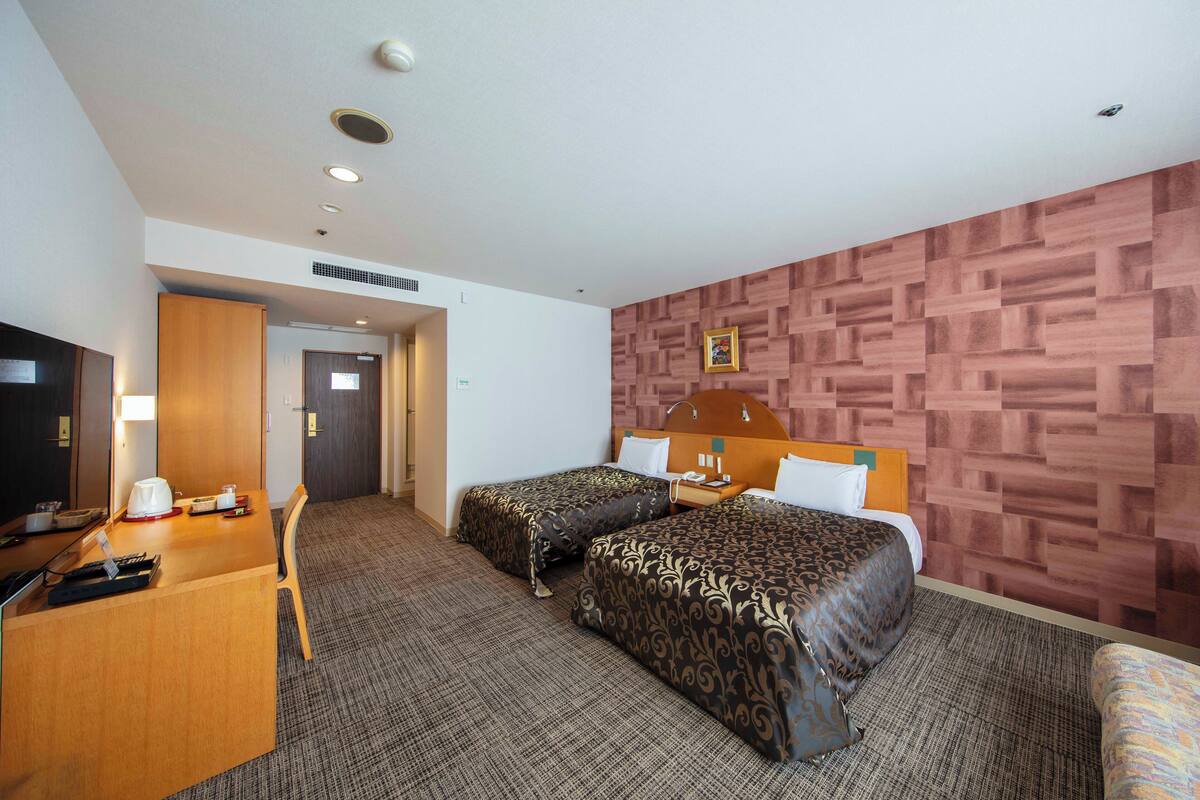 Una habitación de hotel con dos camas, un escritorio con ordenador y teléfono, y una televisión.