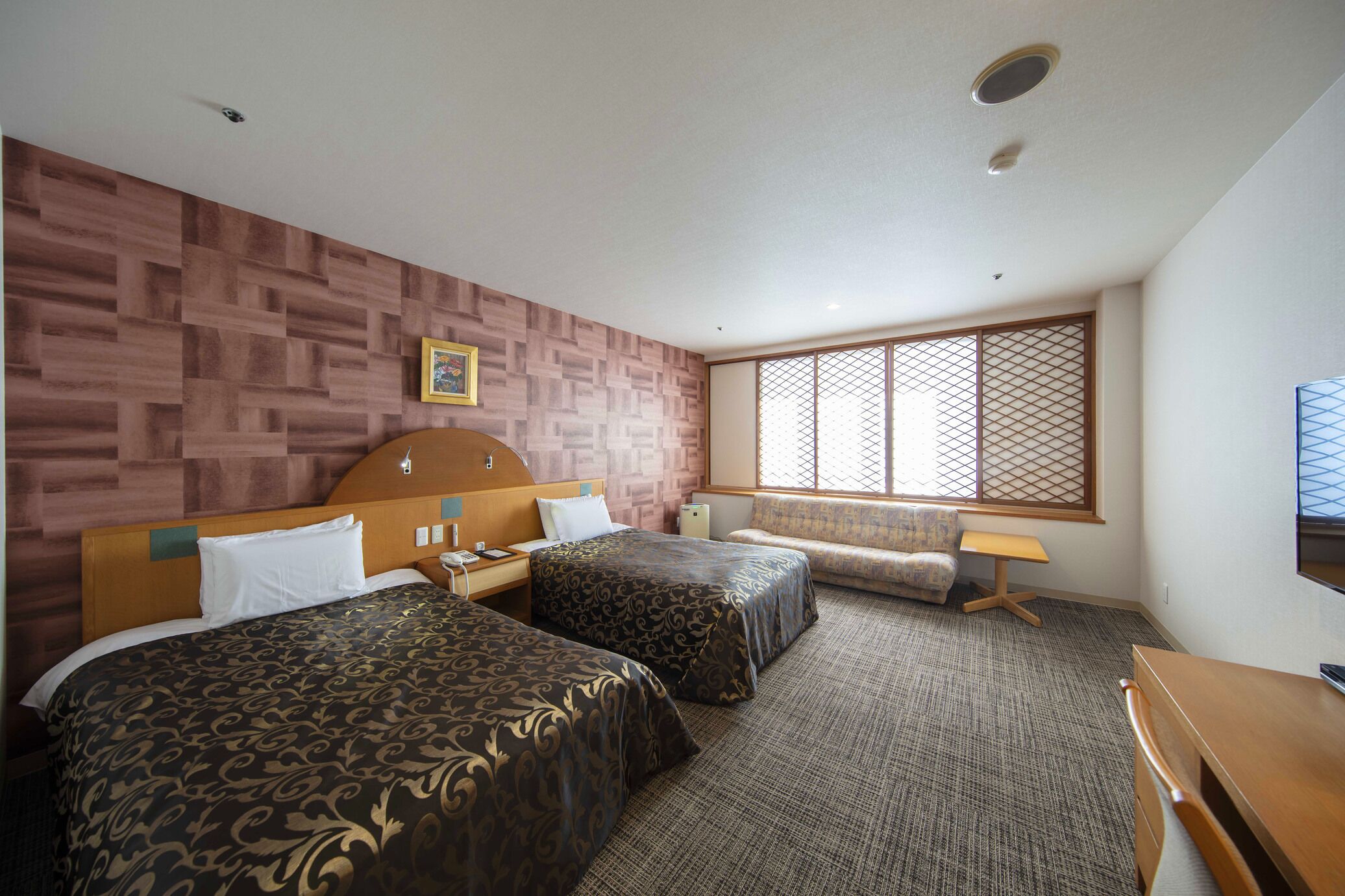A hotel room with two beds, a wooden headboard, a small desk, a chair, and a large window with a view.