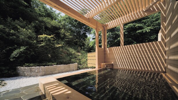 A wooden hot tub with a stone border, surrounded by a wooden pergola and lush greenery. - Santoka - Kurashiki Yuga Onsen - (Kurashiki)