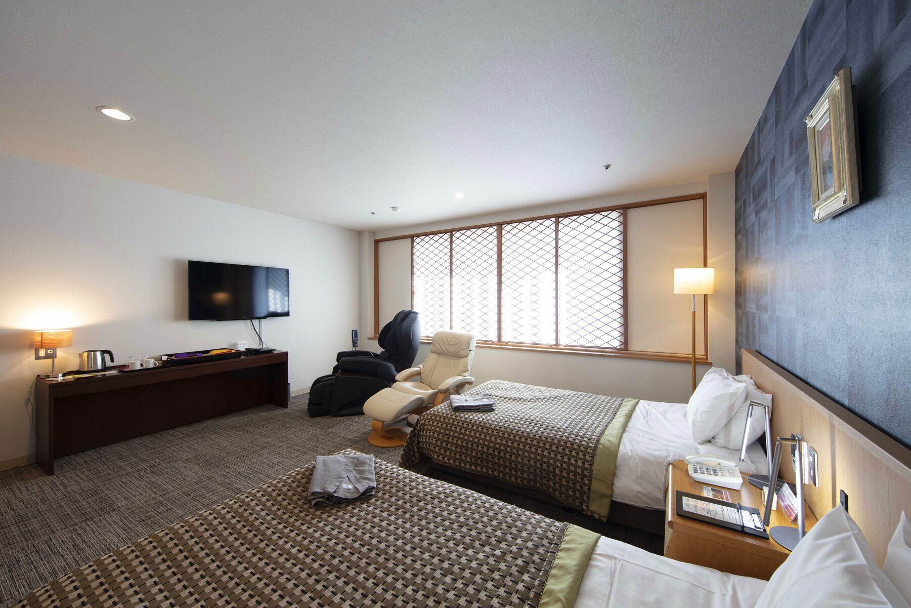 A hotel room with two beds, a desk, a chair, a TV, and a window with a view.