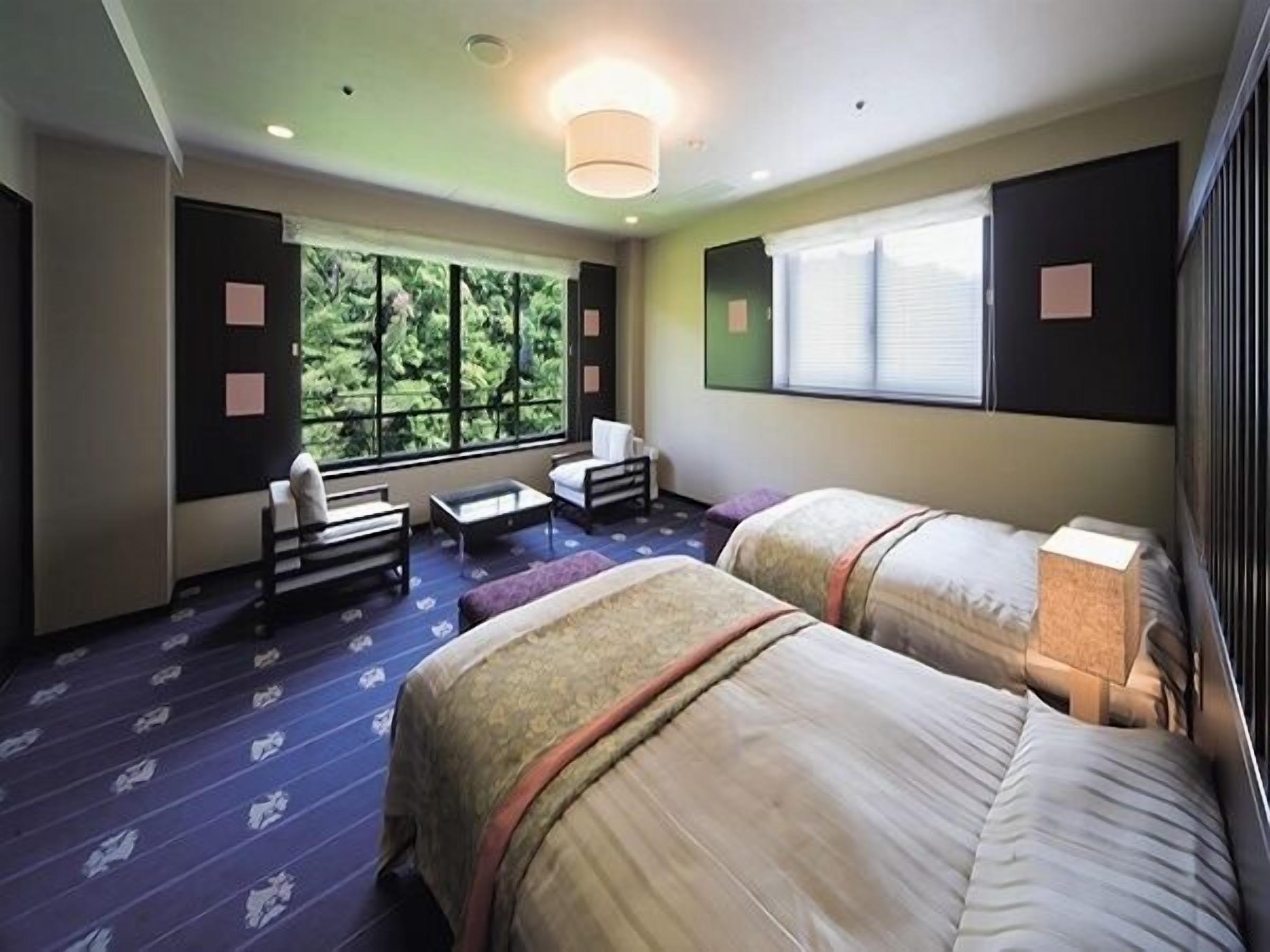 Habitación de hotel con dos camas, un sofá, una mesita y ventana con vistas a zonas verdes.