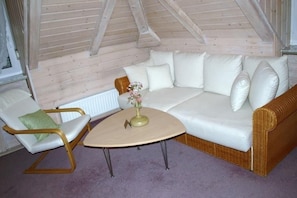 A cozy room with a white sofa, a green chair, and a small round table with a vase. - Hotel Villa Sulmana (Neckarsulm)