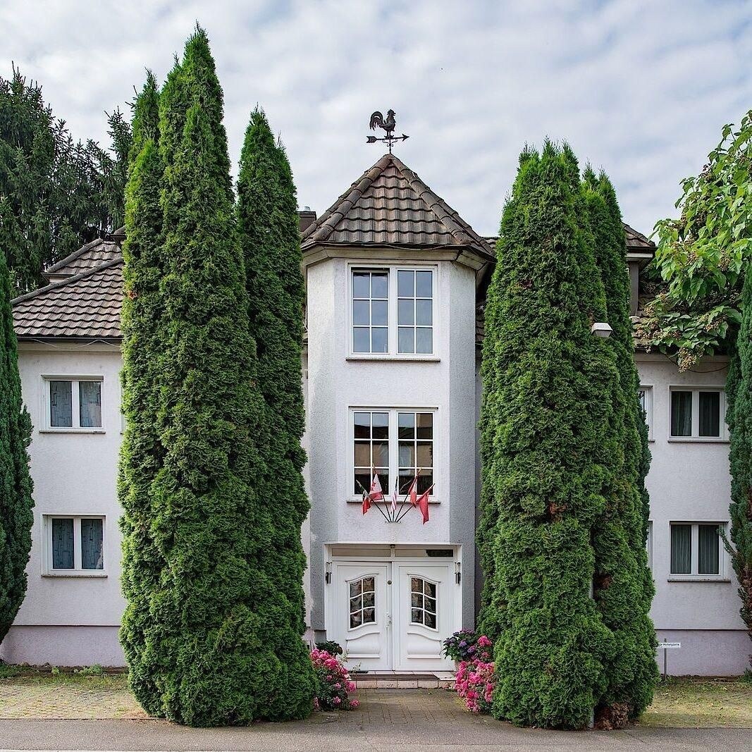 A two-story building with a grey facade, a weather vane on the roof, and a symmetrical window arrangement.