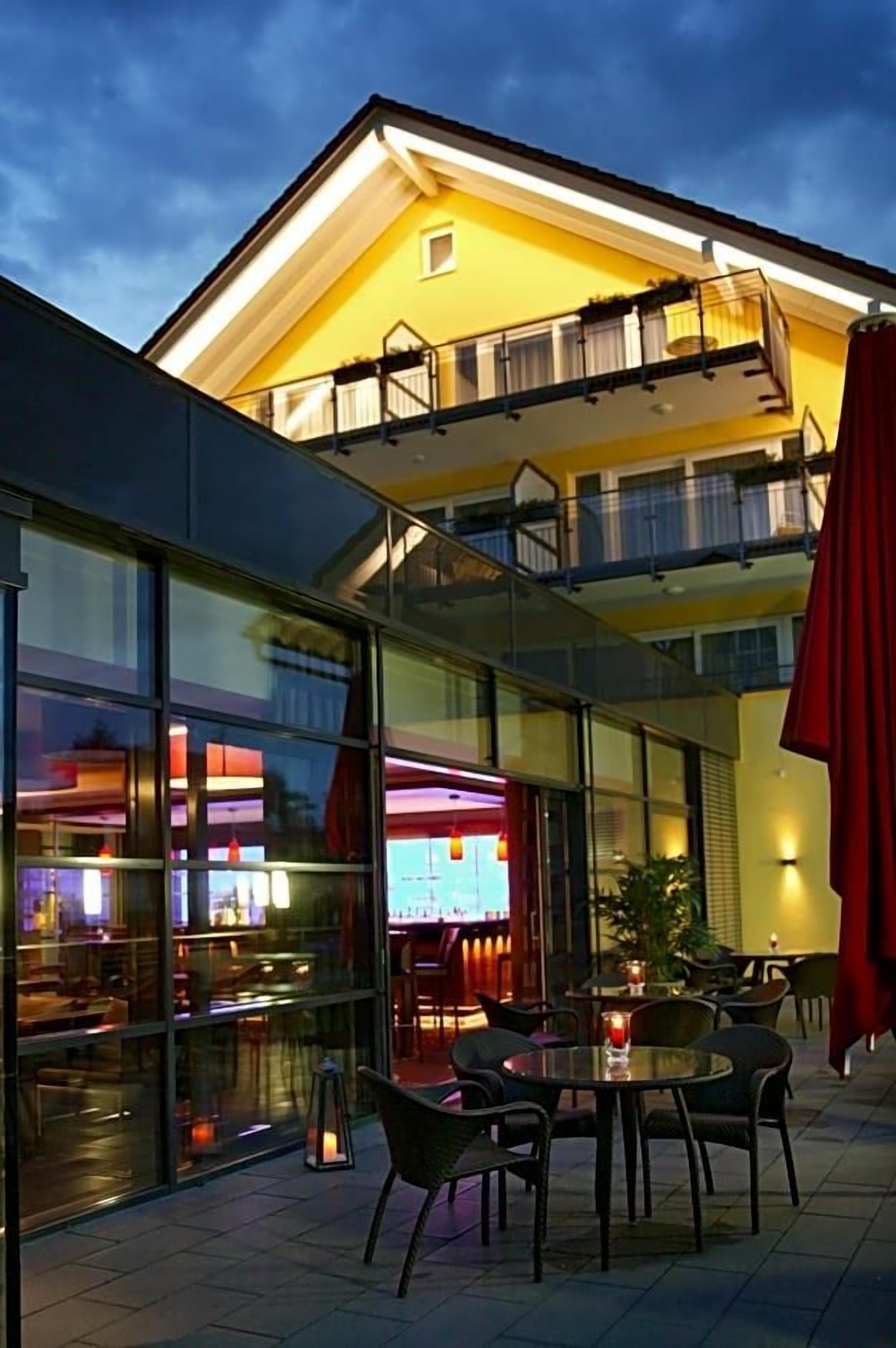 A building with a glass facade, outdoor seating area, and a brightly lit interior.