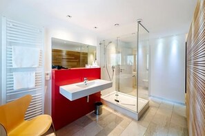 Un baño moderno con cabina de ducha de vidrio, un lavamanos blanco y una pared de acento roja.
