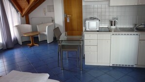 A compact hotel room with a kitchenette, a dining area with a table and chairs, and a bed. - Wo der Hahn Kräht (Flein)