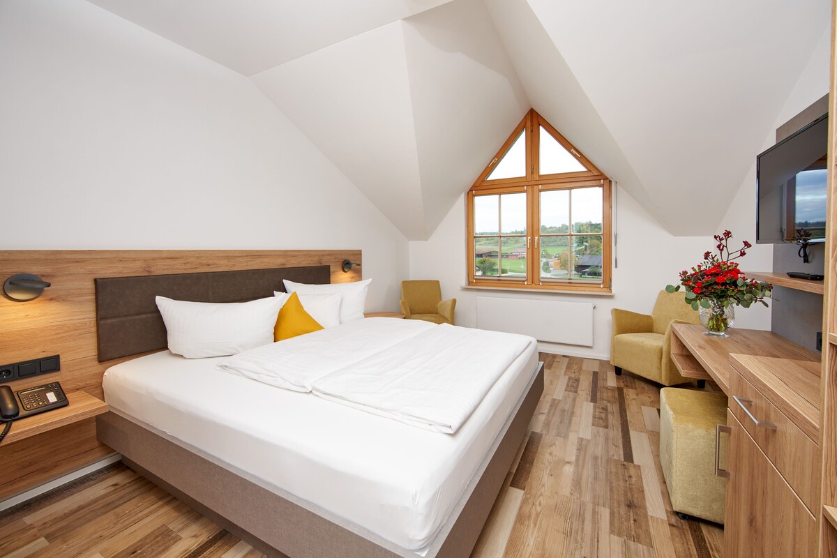 A bedroom with a bed, bedside table, lamp, and a window with a view.