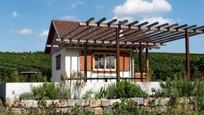 A house with a wooden pergola, a stone wall, and a garden with various plants. - Wo der Hahn Kräht (Flein)