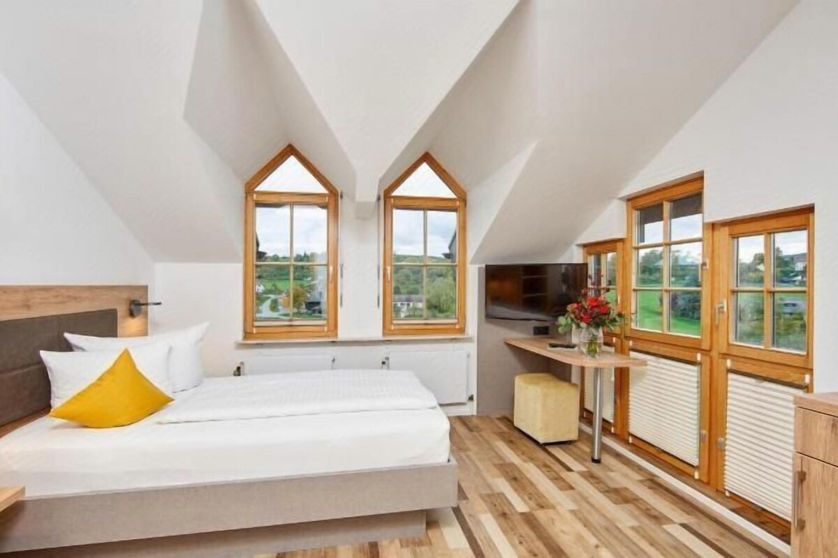 Un dormitorio con cama, mesita de noche, ventana y vistas al exterior.