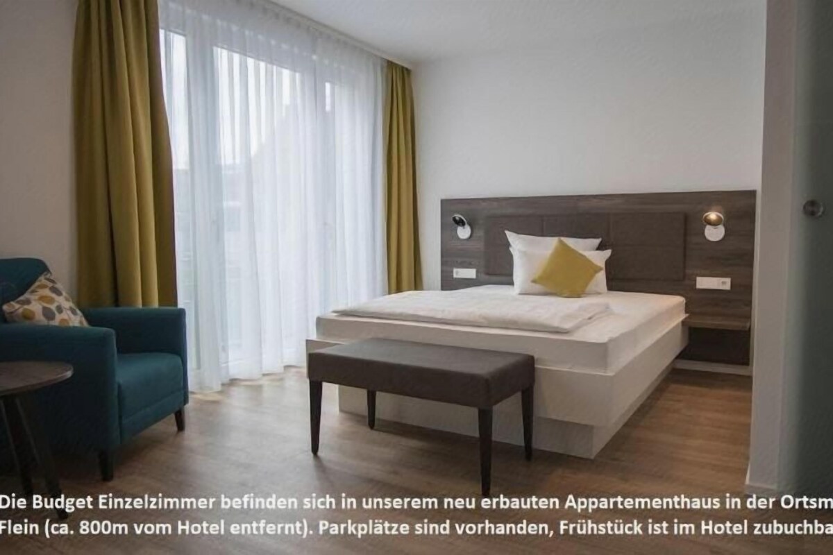 Una habitación de hotel con cama, mesita de noche y una silla.