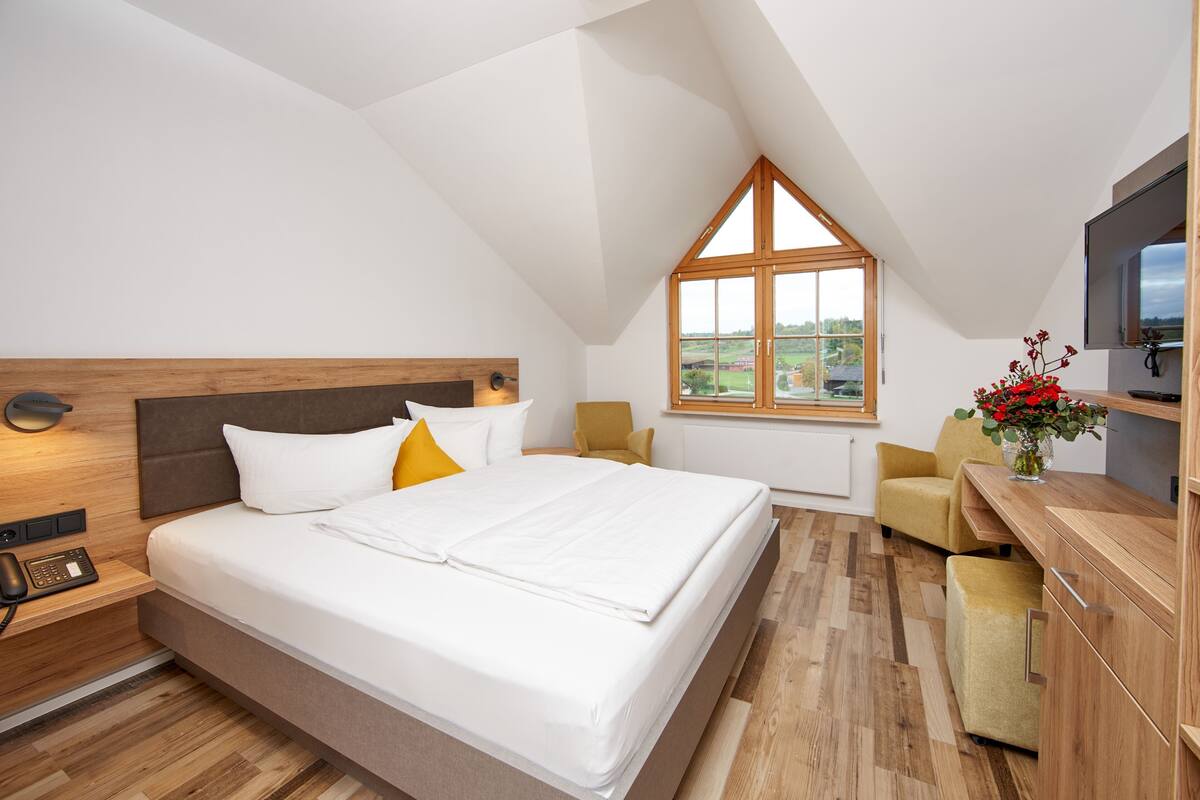 A bedroom with a bed, bedside table, lamp, and a window with a view.