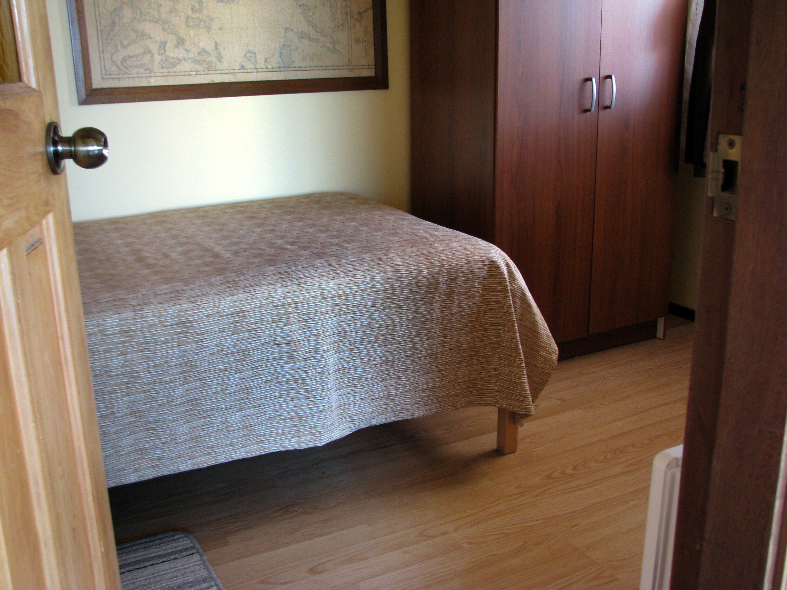 Een slaapkamer met een bed, een houten garderobe en een inlijste kaart aan de muur.