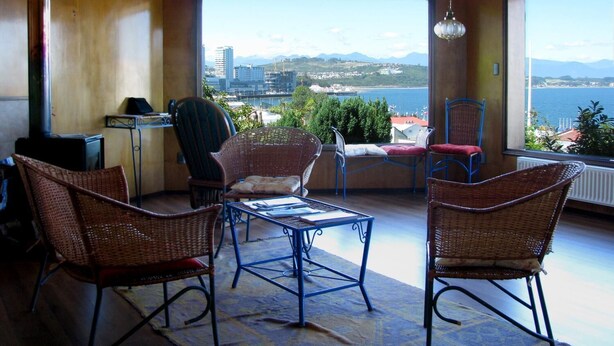 En balkon med fletningsmøbler, et bord og udsigt over by og bjerglandskab.