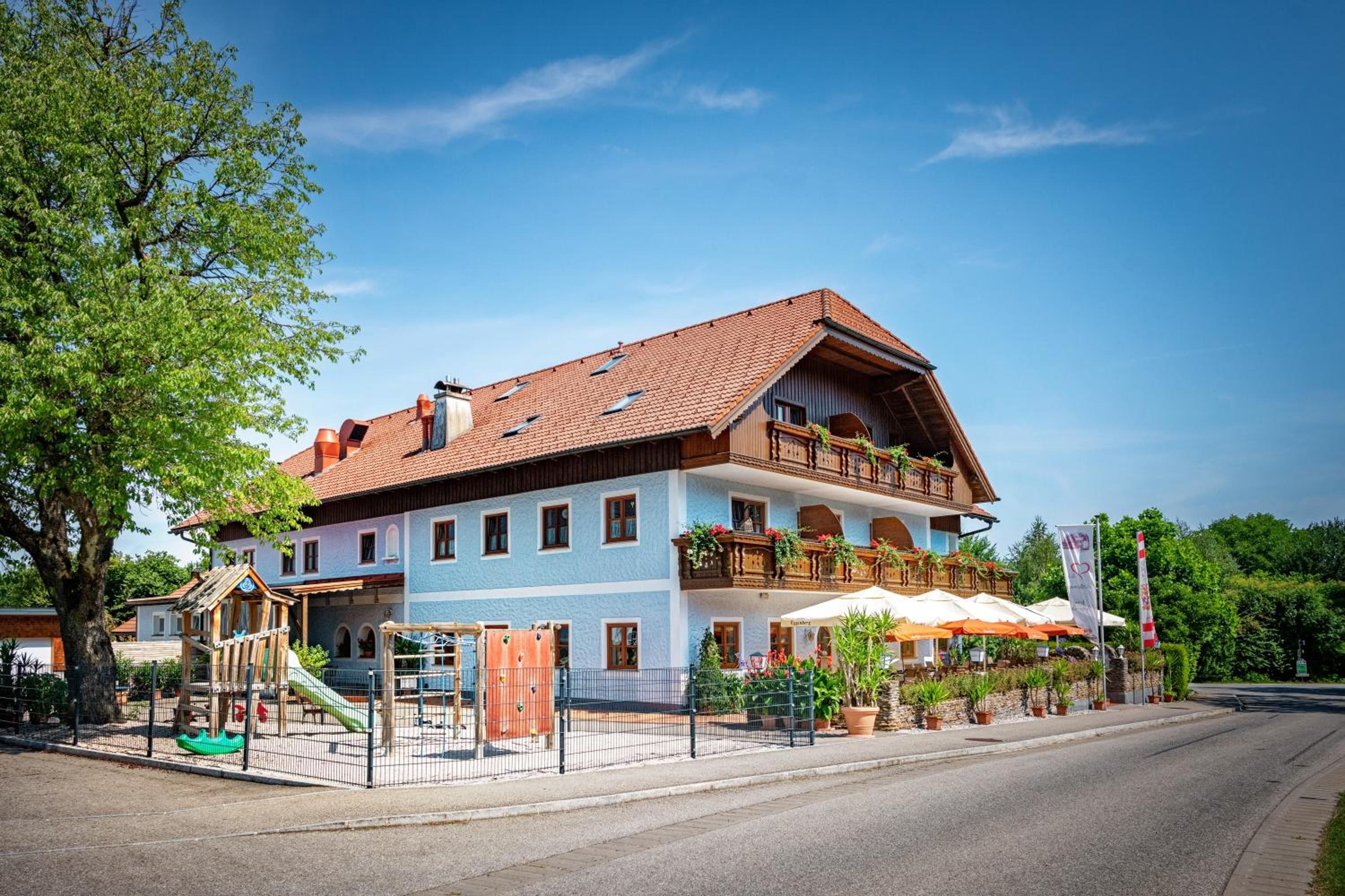 A two-story building with a red-tiled roof, a balcony with plants, and a playground with a slide.