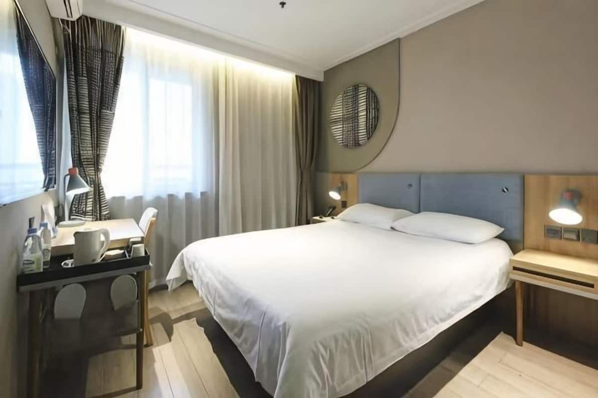 A hotel room with a bed, bedside table, lamp, desk, chair, and curtains.
