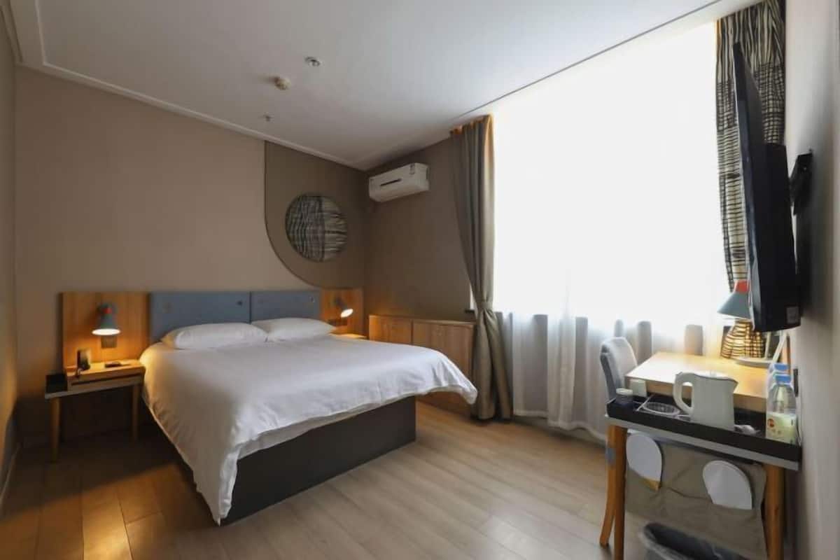 A hotel room with a bed, bedside table, lamp, and a desk with a chair.