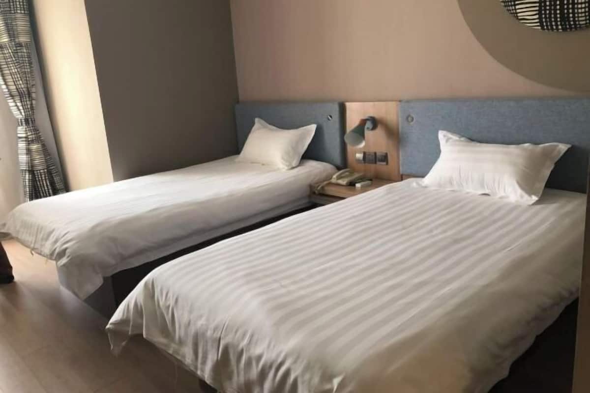 A hotel room with two single beds, a bedside telephone, and a wall-mounted lamp.