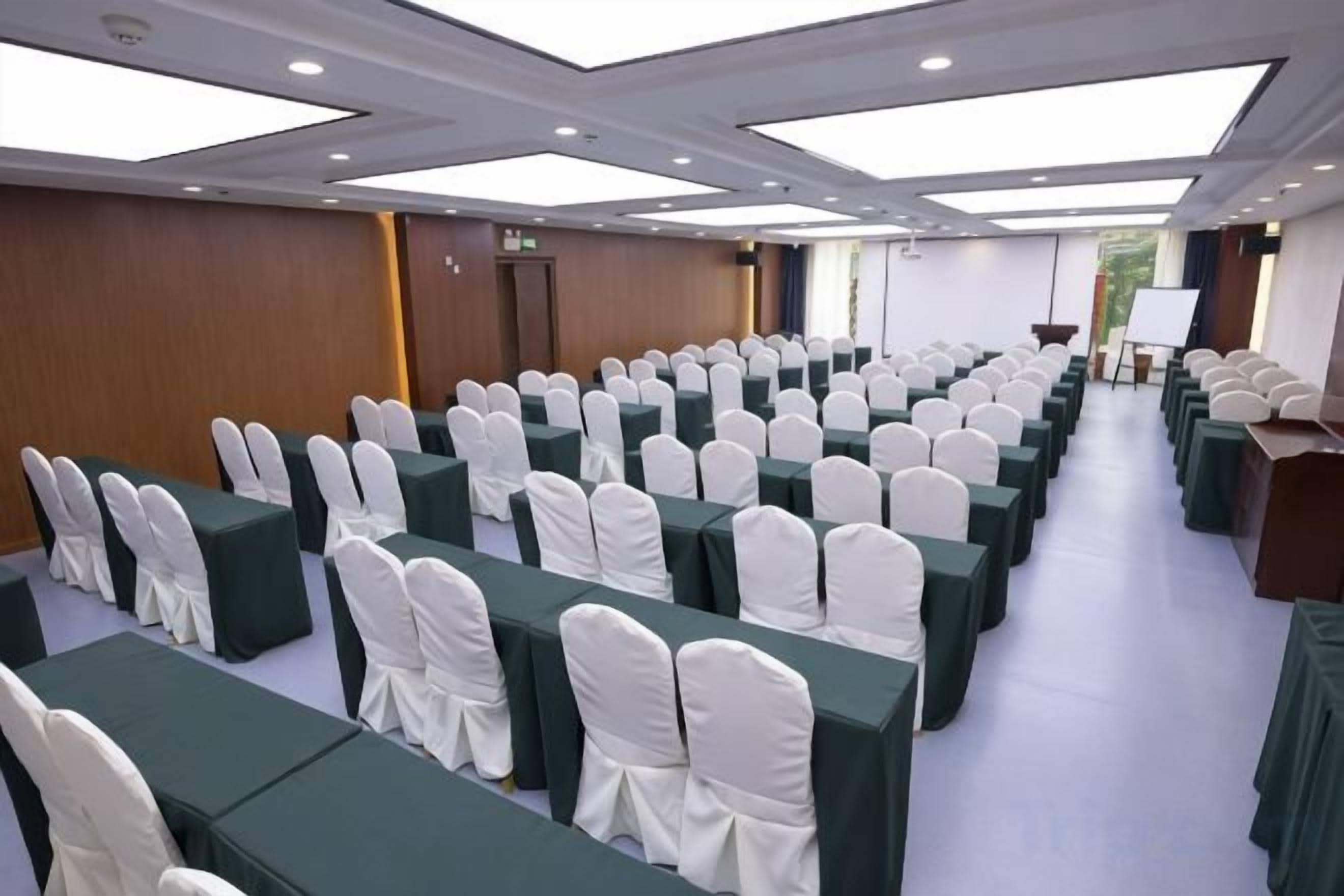 Un salón de conferencias con filas de mesas y sillas, un atril y un amplio ventanal.