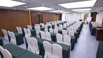 Un salón de conferencias con filas de mesas y sillas, un atril y un amplio ventanal.