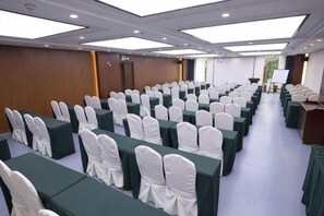 Une salle de conférence avec des rangées de tables et de chaises, un pupitre et une grande fenêtre.