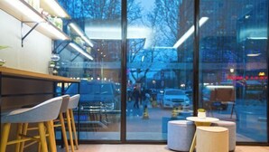 Eine moderne Bar mit Holzhöckern und einer Glaswand, die einen Blick auf die Straße ermöglicht.
