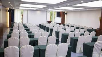 A conference room with rows of tables and chairs, a projector screen, and a presentation podium.