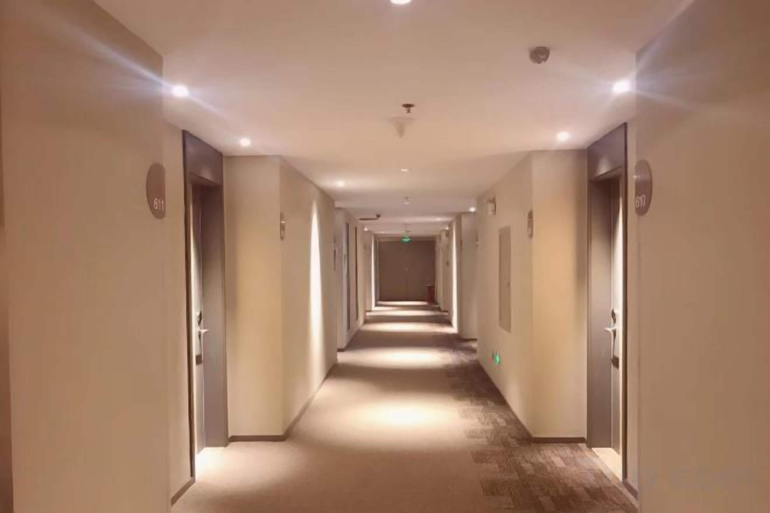 Un pasillo de hotel con puertas a ambos lados, piso alfombrado e iluminación empotrada en el techo.