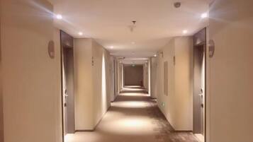 Un pasillo de hotel con puertas a ambos lados, piso alfombrado e iluminación empotrada en el techo.