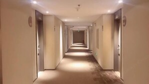Ein langer, schmaler Hotelgang mit Türen an beiden Seiten, eingelassener Beleuchtung und Teppichboden.