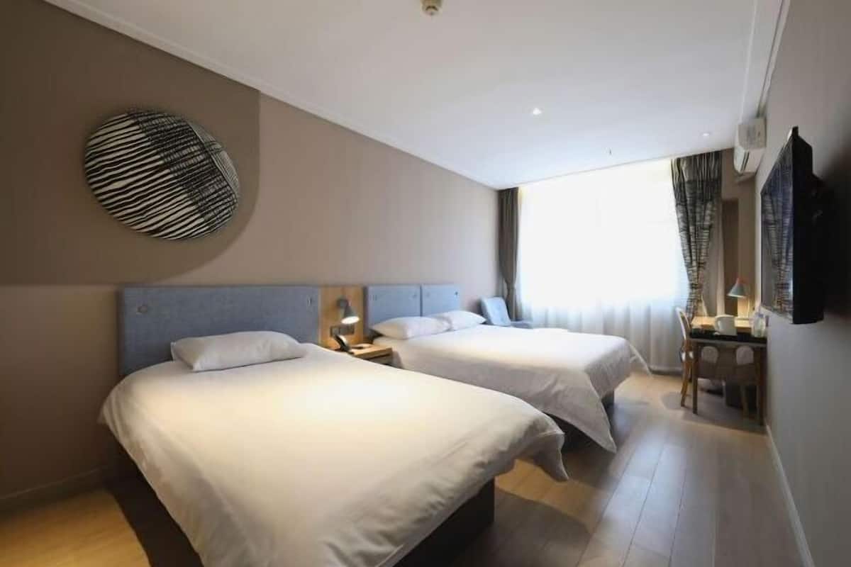A hotel room with two beds, a desk, and a large window.