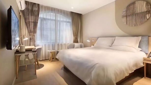 Ein modernes Hotelzimmer mit einem großen Bett, Nachttischen, einem Fernseher und einem Fenster mit Vorhängen.