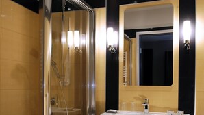 Ein modernes Badezimmer mit einer gläsernen Dusche, einem Waschbecken mit Spiegel und schwarzen und goldenen Fliesenwänden.