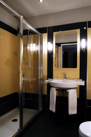 Ein modernes Badezimmer mit einer gläsernen Dusche, einem Waschbecken mit Spiegel und schwarzen und goldenen Fliesenwänden.