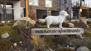 Schild für die Mackenzie Apartments mit einer Steinskulptur eines Schafs davor.
